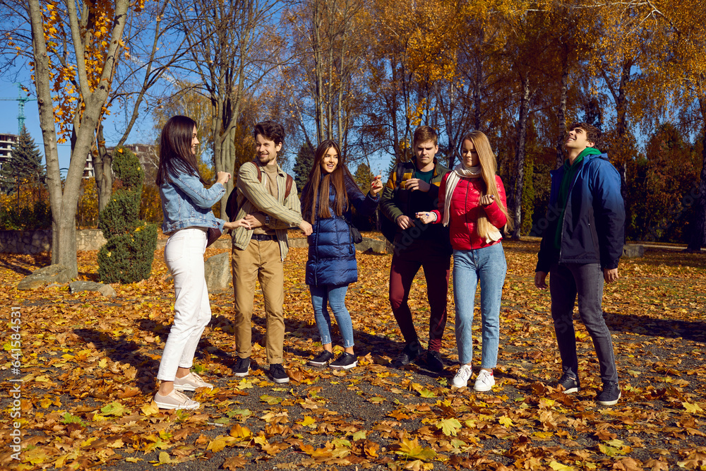Joint activity in the form of games of happy young people in park on sunny, clear day, holding hands against the background of autumn forest. Cheerful smiling friends are enjoying autumn walk in park. Joint activity in the form of games of happy young people in park on sunny, clear day, holding hands against the background of autumn forest. Cheerful smiling friends are enjoying autumn walk in park.