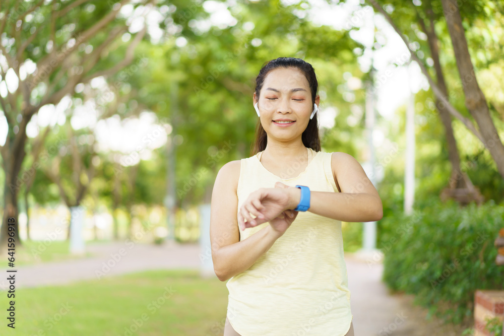Beautiful smart and good looking Asian adult woman checking on a smartwatch or fitness tracker while practicing running - jogging at the park. Fitness tracker and healthcare technology concept. Beautiful smart and good looking Asian adult woman checking on a smartwatch or fitness tracker while practicing running - jogging at the park. Fitness tracker and healthcare technology concept.