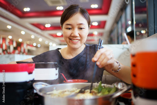 Happy - cheerful Asian fat woman enjoy eating a traditional Asian Hotpot or Sukiyaki in the Asian Hotpot restaurant.