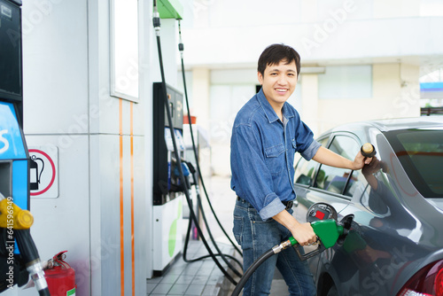 Happy cheerful Asian middle adult man refueling his car at self-service gas station, man refilling his vehicle gas at the gas station.