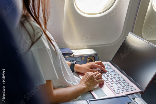Business woman commercial plane passenger using laptop on board for working while sitting in airplane. Traveling and technology image concept.
