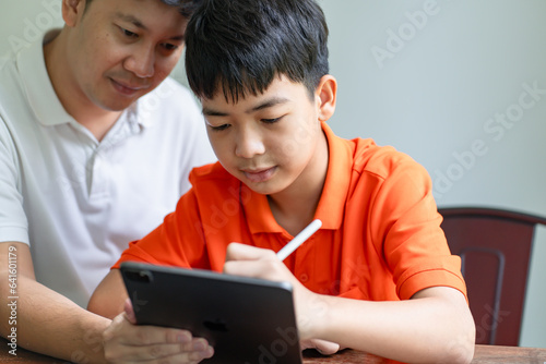 Asian father and son using tablet teaching son to draw.playing with digital tablet at desk fatherhood