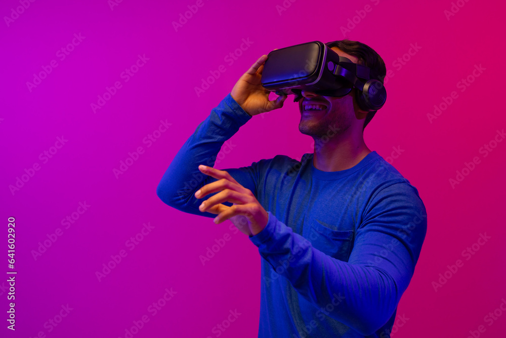 Biracial businessman using vr headset and pointing with fingers on neon pink to purple background Biracial businessman using vr headset and pointing with fingers on neon pink to purple background