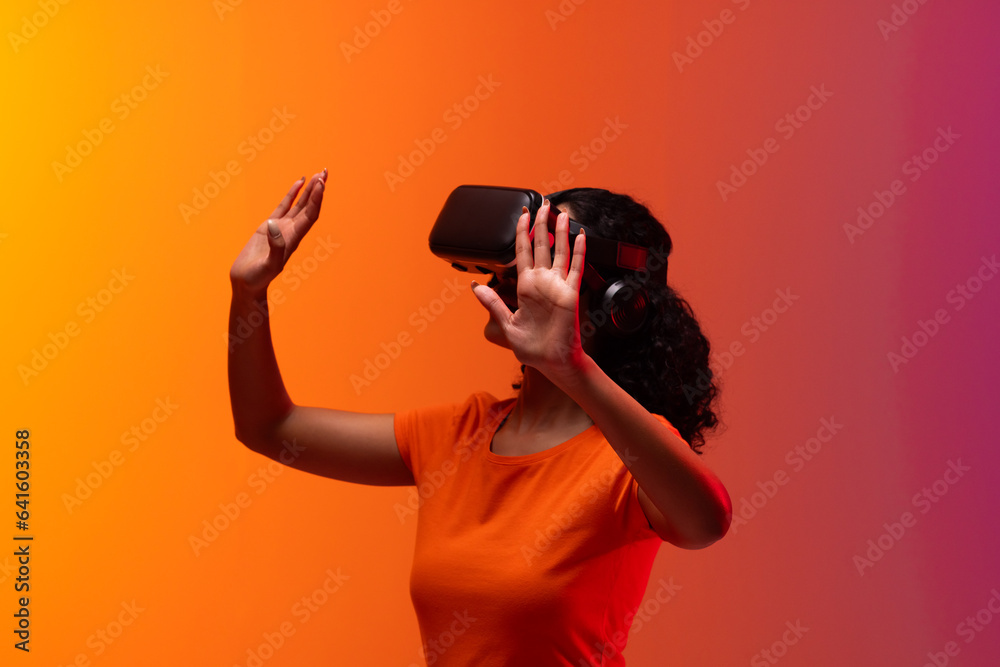 Biracial woman using vr headset and pointing on neon red to orange background Biracial woman using vr headset and pointing on neon red to orange background