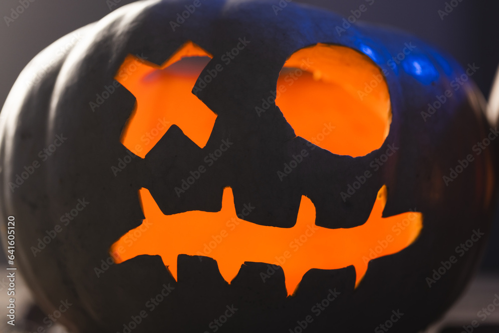 Fototapeta premium Carved pumpkin face illuminating with orange light on black background