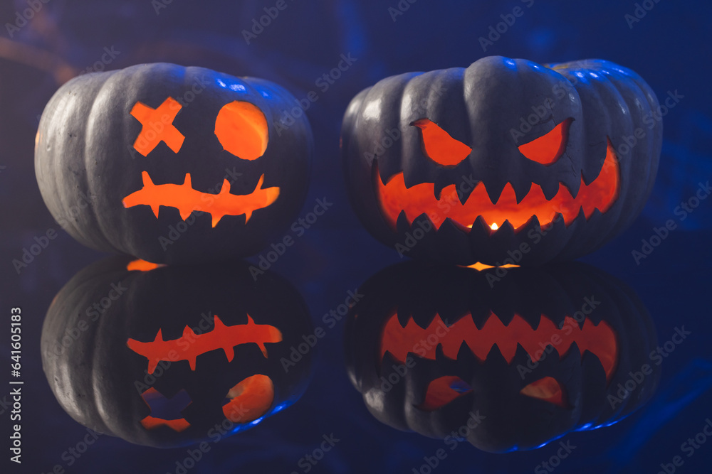 Fototapeta premium Two black carved pumpkins faces on blue background