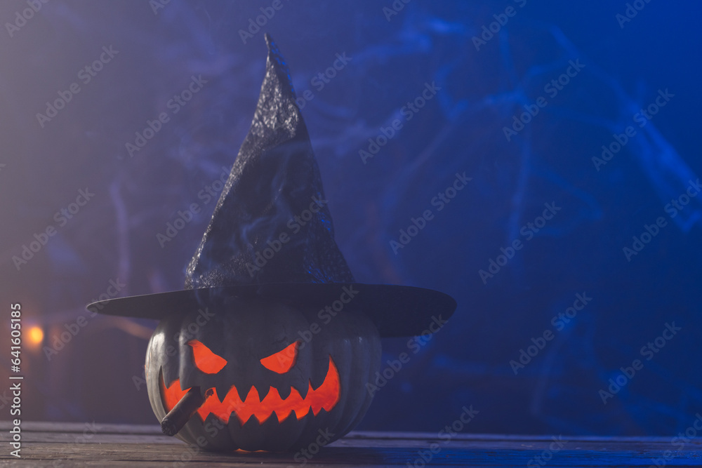 Fototapeta premium Carved pumpkin wearing witch hat with copy space on blue background