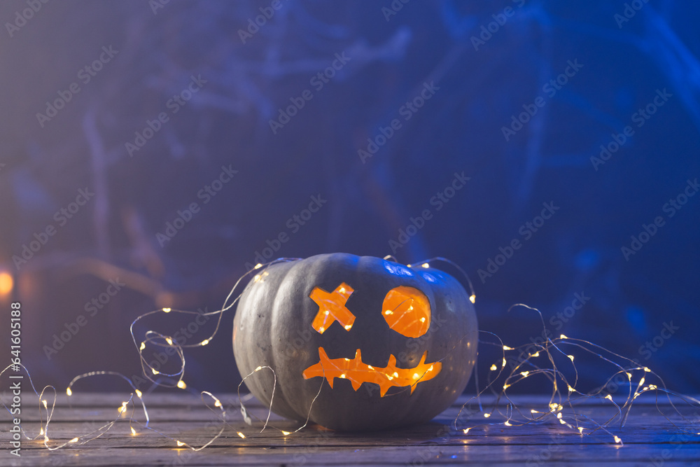 Fototapeta premium Carved pumpkin with led lights with copy space on blue background