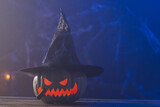 Carved pumpkin wearing witch hat with copy space on blue background