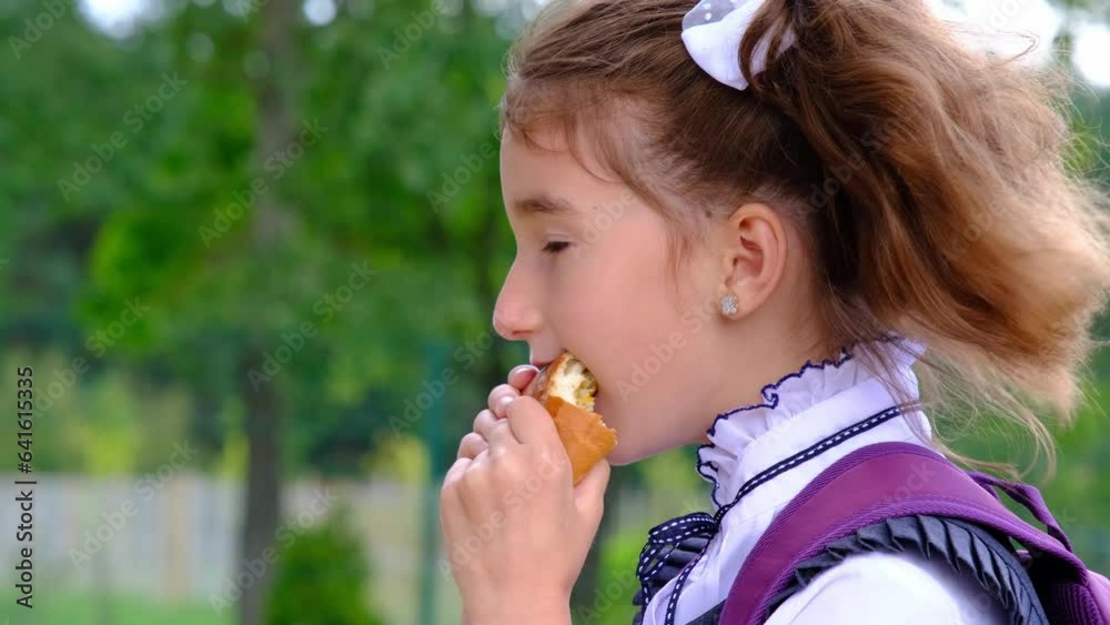 Girl with a backpack eating pie near school. A quick snack with a bun, unhealthy food, lunch from school. Back to school. Education, primary school classes, September 1 Girl with a backpack eating pie near school. A quick snack with a bun, unhealthy food, lunch from school. Back to school. Education, primary school classes, September 1