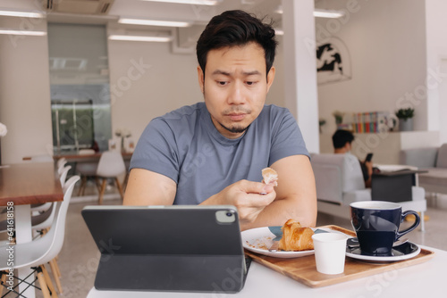 Asian man sitting working drinking coffee with tablet at cafe.