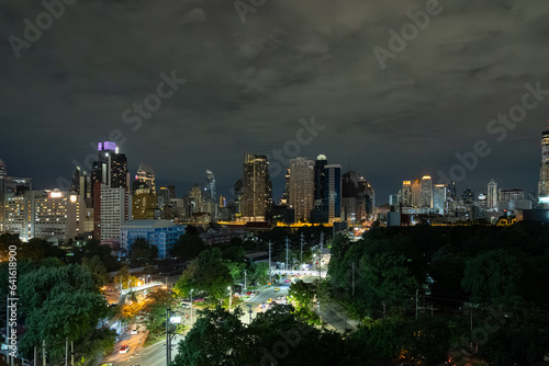 Lights of cityscape and street with busy traffic near downtown of Bangkok at night under a cloudy sky.