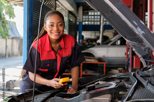 One Black female professional automotive mechanical worker checks an EV car battery and hybrid engine at a maintenance garage, expert electric vehicle service, and fixing occupations auto industry. © tigercat_lpg