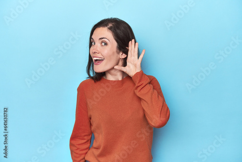 Schilderij op canvas Young caucasian woman on blue backdrop trying to listening a gossip