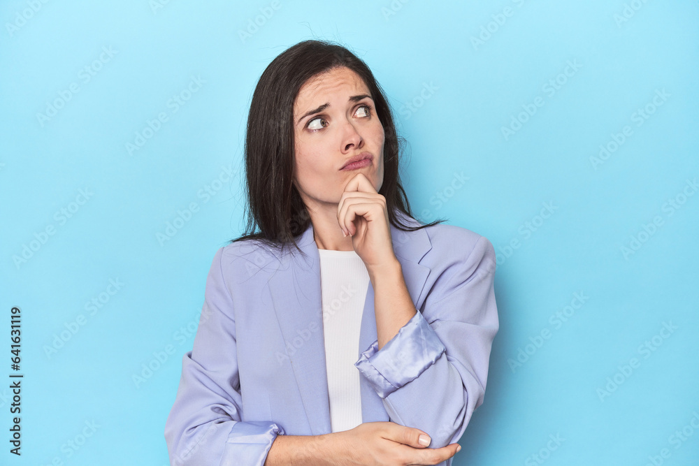 Woman in blue blazer on blue background thinking and looking up, being reflective, contemplating, having a fantasy. Woman in blue blazer on blue background thinking and looking up, being reflective, contemplating, having a fantasy.