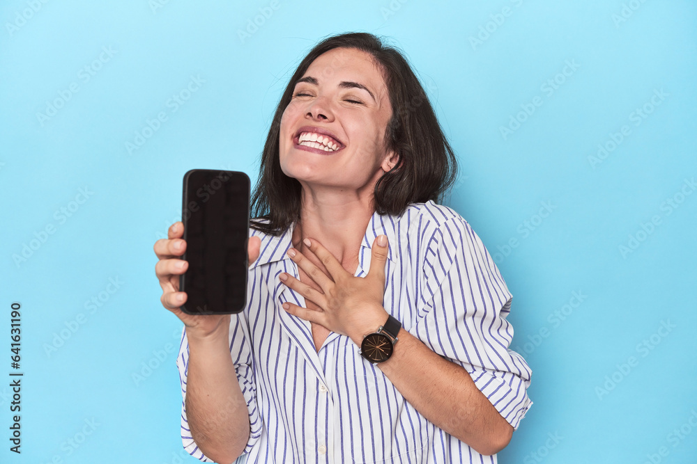 Hopeful woman displaying phone screen on blue Hopeful woman displaying phone screen on blue