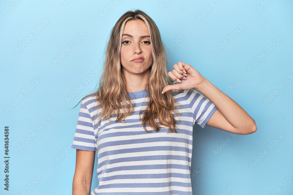 Blonde young caucasian woman in blue studio showing thumb down, disappointment concept. Blonde young caucasian woman in blue studio showing thumb down, disappointment concept.