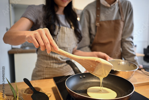 Shot of housewife pouring pancake batter into frying pan, preparing breakfast in cozy kitchen