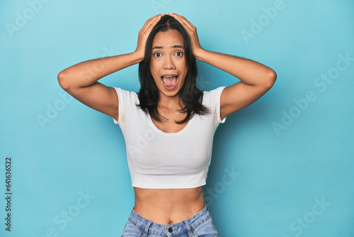 Filipina young woman on blue studio screaming, very excited, passionate, satisfied with something.