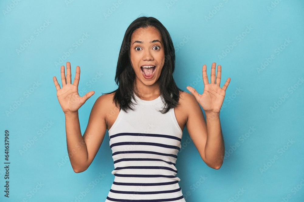 Filipina young woman on blue studio receiving a pleasant surprise, excited and raising hands. Filipina young woman on blue studio receiving a pleasant surprise, excited and raising hands.