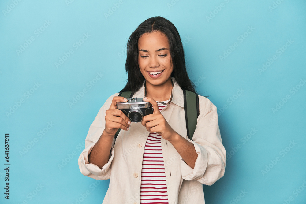 Young Filipina capturing moments with camera on a blue studio backdrop Young Filipina capturing moments with camera on a blue studio backdrop