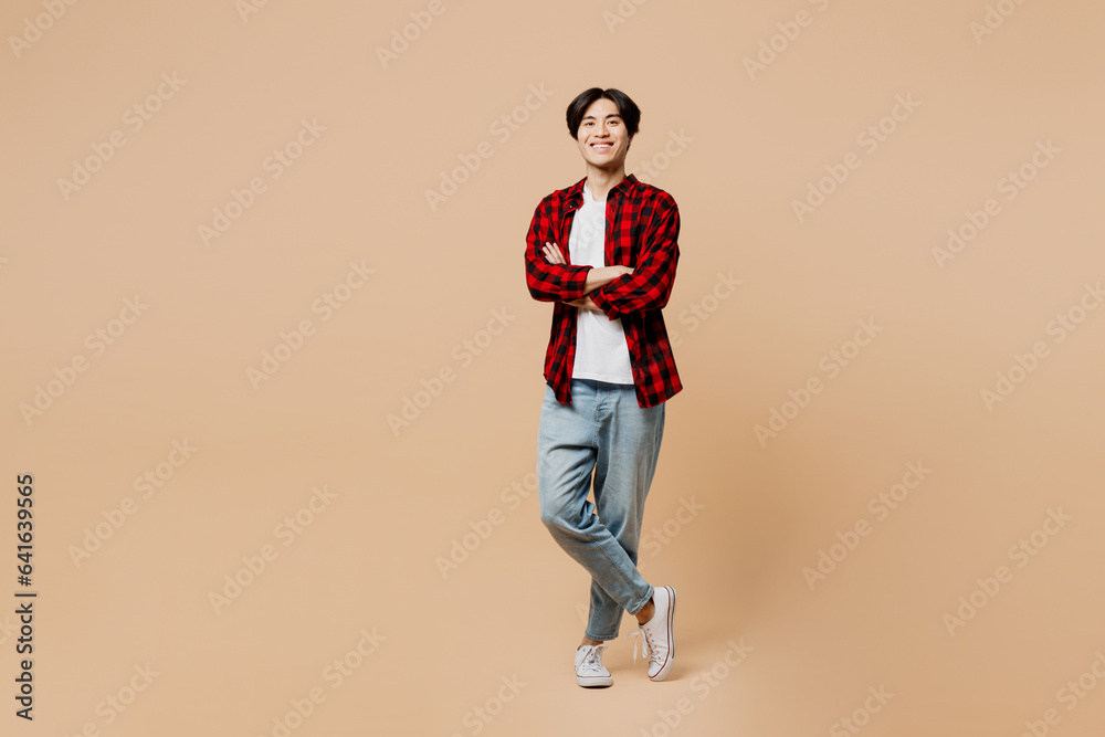 Full body young happy confident man of Asian ethnicity he wear red shirt casual clothes look camera hold hands crossed folded isolated on plain pastel light beige background studio. Lifestyle concept. Full body young happy confident man of Asian ethnicity he wear red shirt casual clothes look camera hold hands crossed folded isolated on plain pastel light beige background studio. Lifestyle concept.