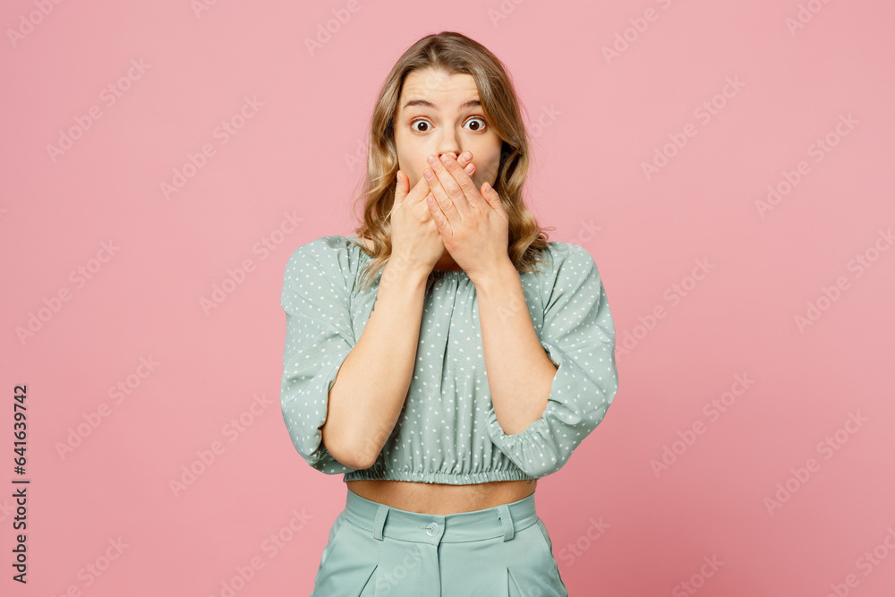 Young shocked scared astonished fearful amazed stupefied woman wear casual clothes look camera cover mouth with hands isolated on plain pastel light pink background studio portrait. Lifestyle concept.