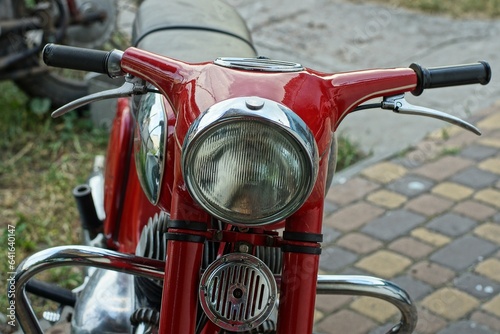 the front of the old original iron red with a glass headlight, steering wheel and signal of a heavy classic java motorcycle stands on the street in the summer afternoon