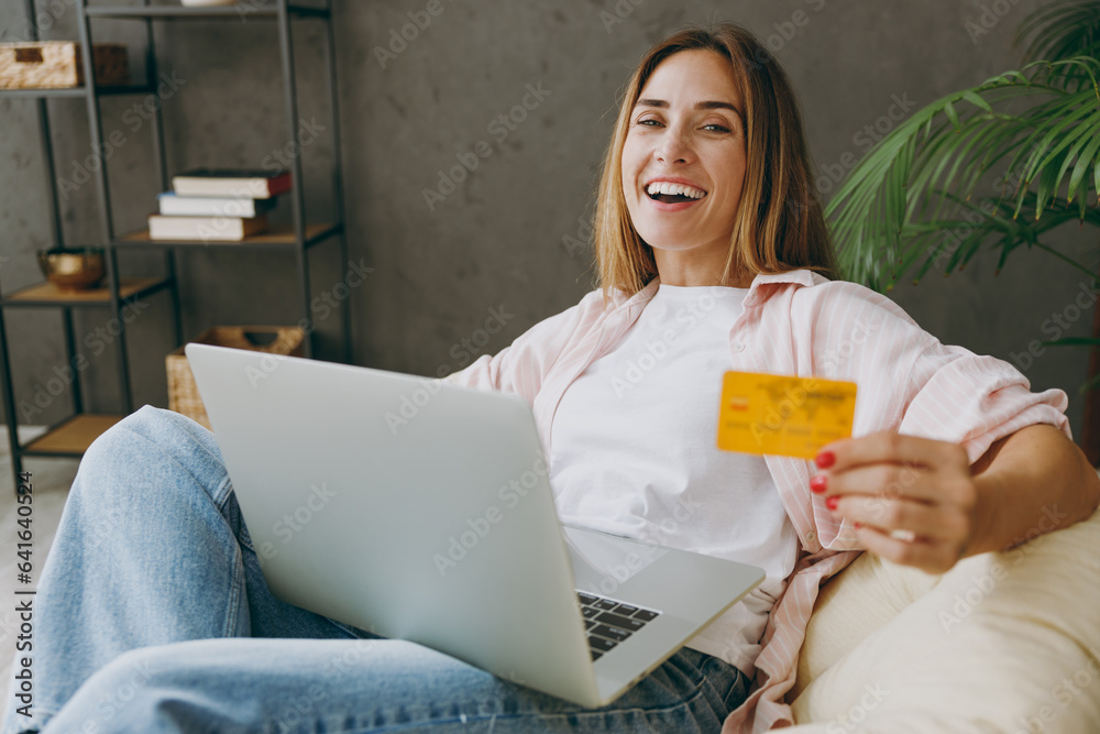 Young IT woman wears casual clothes sits in armchair use laptop pc computer credit bank card shopping online stay home hotel flat rest relax spend free spare time in living room indoor Lounge concept Young IT woman wears casual clothes sits in armchair use laptop pc computer credit bank card shopping online stay home hotel flat rest relax spend free spare time in living room indoor Lounge concept