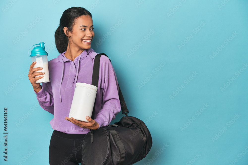 Filipina athlete with protein shake and powder on blue studio Filipina athlete with protein shake and powder on blue studio