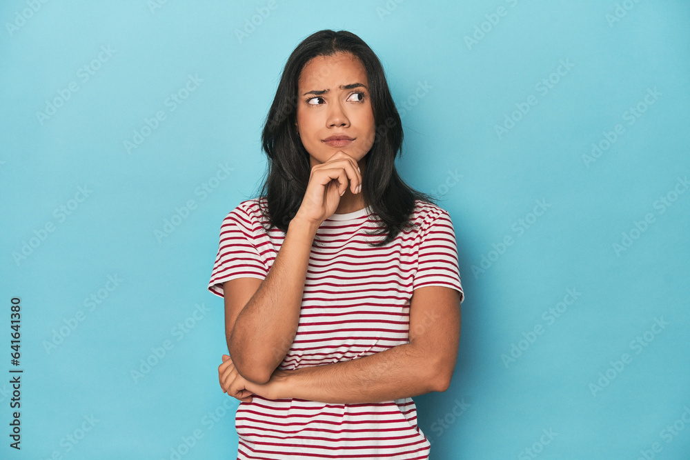 Filipina young woman on blue studio thinking and looking up, being reflective, contemplating, having a fantasy. Filipina young woman on blue studio thinking and looking up, being reflective, contemplating, having a fantasy.