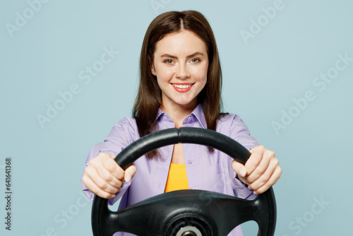 Young happy smiling confident woman wears purple shirt yellow t-shirt casual clothes hold steering wheel driving car isolated on plain pastel light blue background studio portrait. Lifestyle concept.