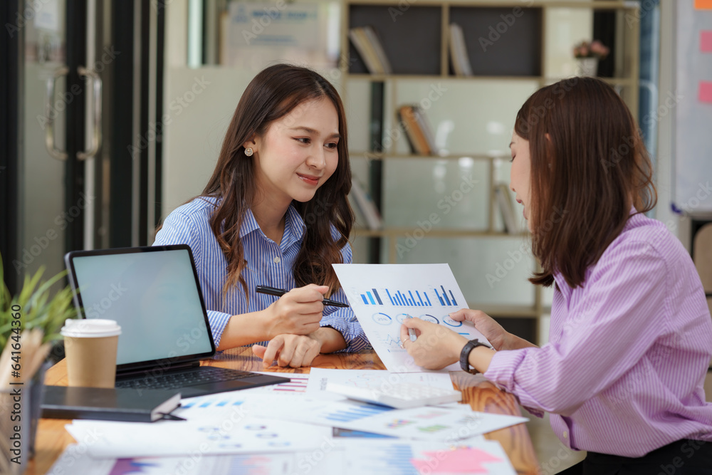 Two Asian businesswomen discussing market data graphs and company data charts, new investment projects, and strategic planning using a tablet at work. Two Asian businesswomen discussing market data graphs and company data charts, new investment projects, and strategic planning using a tablet at work.