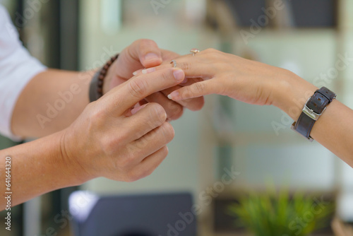 A young man's hand carefully puts a ring on a woman's finger.