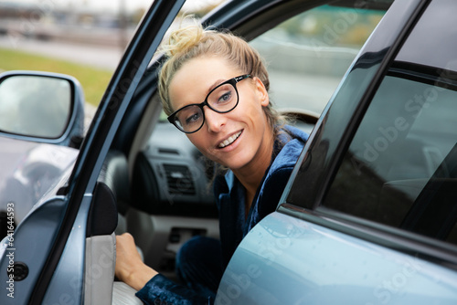 Beautiful woman in glasses looks back over her shoulder as she exits a parked car in which she drove