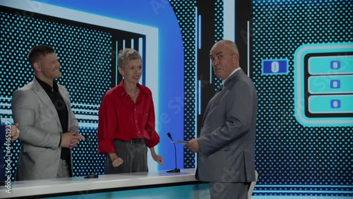 Funny charismatic host talking to the contestants during recording of a fictional morning family game show, guest guessing the right answer