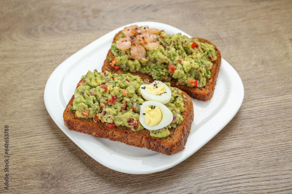 Slices of bread with tasty guacamole, eggs and shrimp on wooden table, closeup