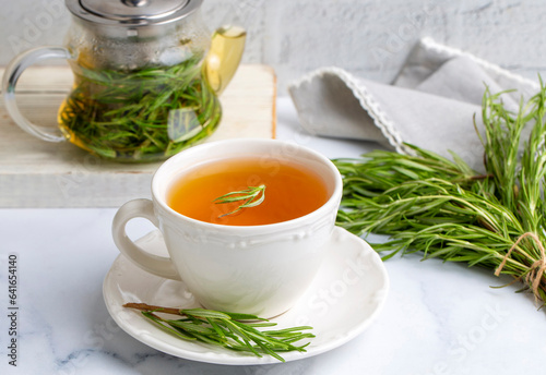 Cup of healthy rosemary tea with fresh rosemary bunch on rustic background, winter herbal hot drink concept, salvia rosmarinus