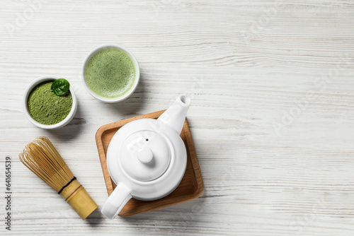 Cup of fresh matcha tea, bamboo whisk, teapot and green powder on white wooden table, flat lay. Space for text
