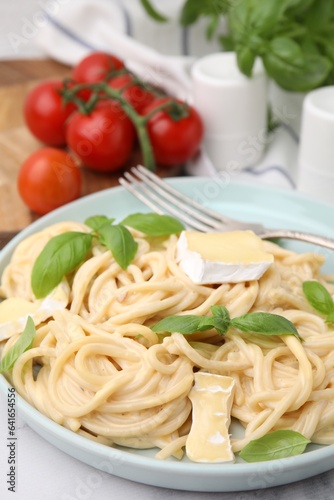 Delicious pasta with brie cheese and basil leaves on table, closeup