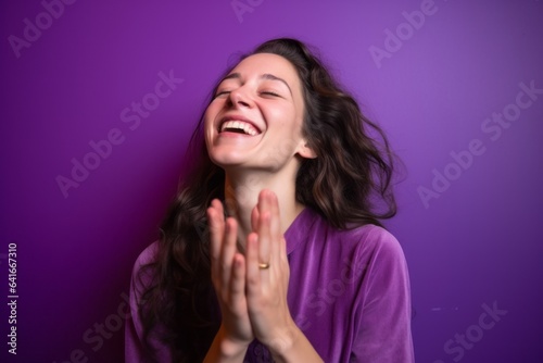 Medium shot portrait photography of a joyful girl in her 30s joining palms in a gesture of gratitude against a vibrant purple background. With generative AI technology