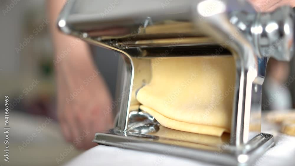 Woman rolls out the dough using a pasta dough rolling machine. Woman rolls out the dough using a pasta dough rolling machine.