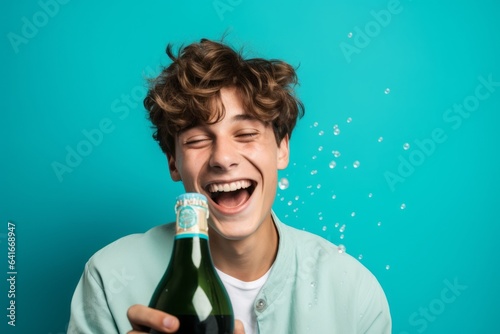 Lifestyle portrait photography of a happy boy in his 20s uncorking a bottle of champagne against a turquoise blue background. With generative AI technology