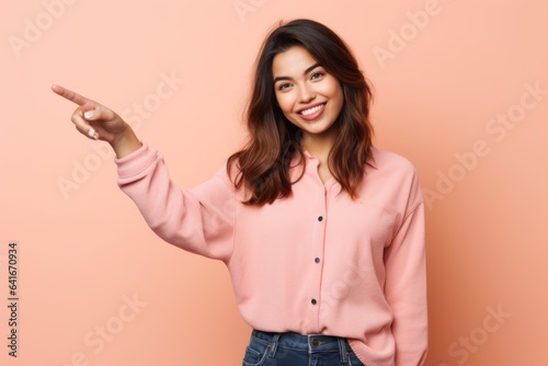 Lifestyle portrait photography of a glad girl in her 30s pointing empty space against a peachy pink background. With generative AI technology