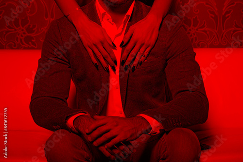 Woman hands with touchning rich man on sofa in red light in nightclub