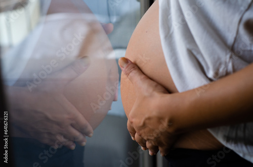 Reflection in the glass of the belly of a pregnant woman. Pregnant woman at 35 weeks gestation. Concept of healthy pregnancy and love and tenderness photo