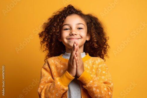Close-up portrait photography of a satisfied kid female joining palms in a gesture of gratitude against a bright yellow background. With generative AI technology