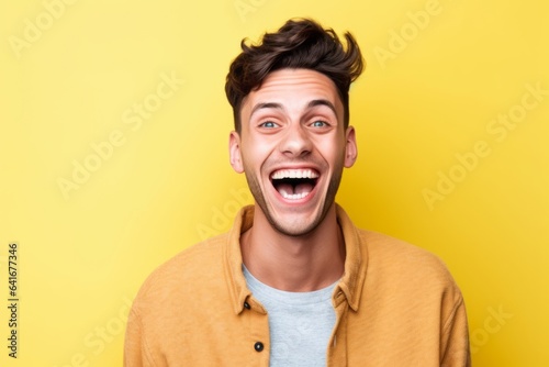 Headshot portrait photography of a glad boy in his 20s placing the hand over the mouth in a laughter gesture against a pastel yellow background. With generative AI technology © Markus Schröder