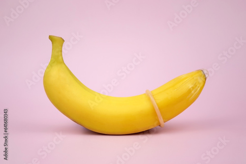 Condom and banana on a pink background close-up.