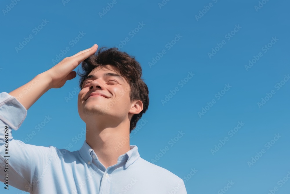 Medium shot portrait photography of a grinning boy in his 20s putting the hand on the forehead to look for someone in the distance against a sky-blue background. With generative AI technology Medium shot portrait photography of a grinning boy in his 20s putting the hand on the forehead to look for someone in the distance against a sky-blue background. With generative AI technology